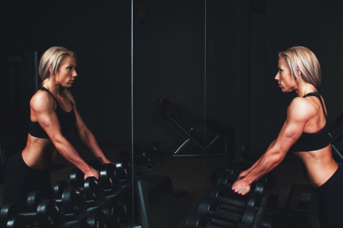 A lifter setting up over dumbbells beside a gym mirror